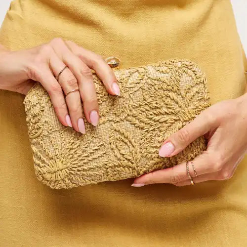 natural woven textured clutch held by a person wearing a yellow outfit